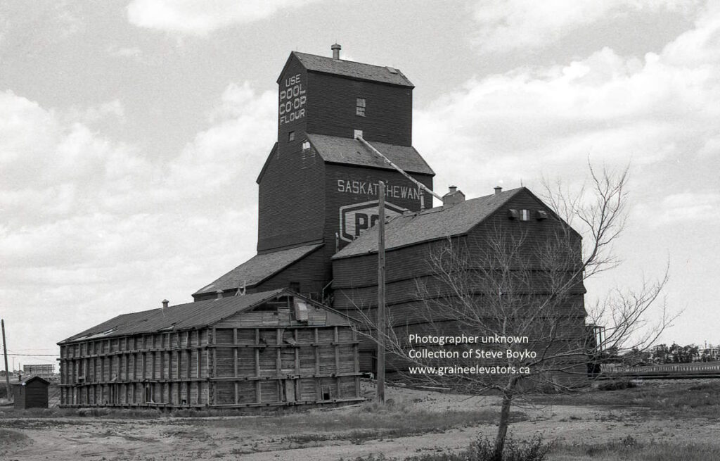 Black and white photograph of wooden grain elevator labeled "Saskatchewan Pool" with the words "Use Pool Co-Op Flour" on the top.