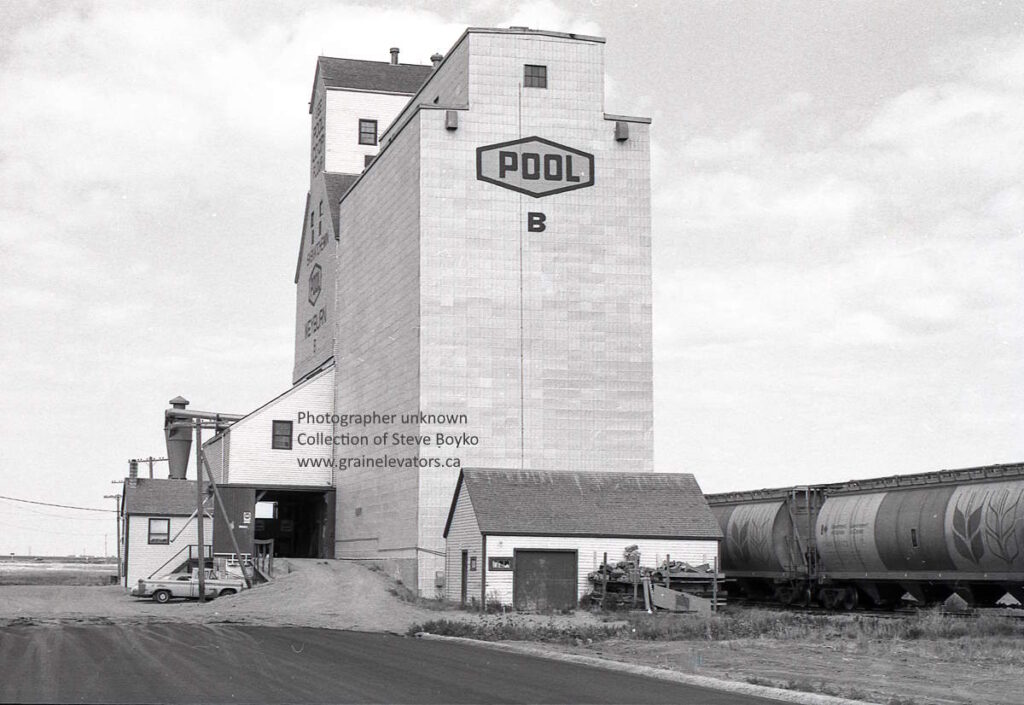 Black and white photograph of a wooden grain elevator with rail cars beside it.
