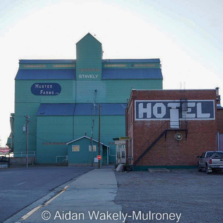 Backlit photo of a green grain elevator and a brick building lettered HOTEL.