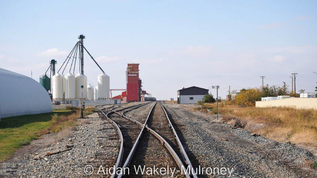 Track receding from view, with a red grain elevator and other buildings in the distance.