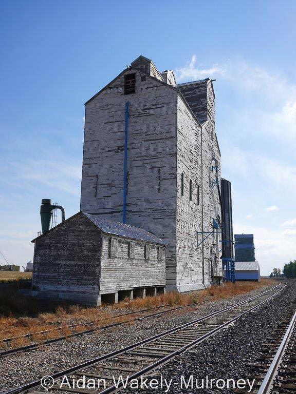Tall and faded white grain elevator by railway tracks