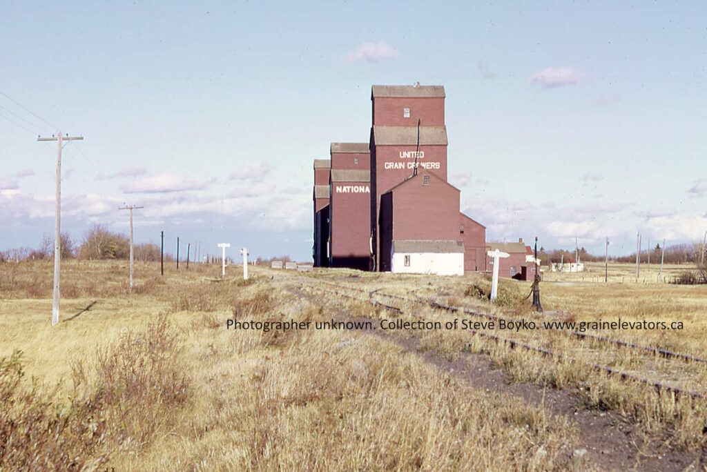 Brown wooden grain elevators on the prairie with railway tracks in front