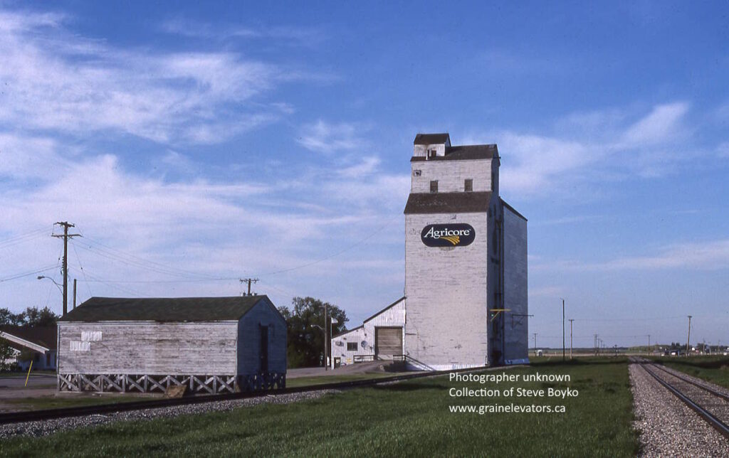 Wooden grain elevator beside railway track with "Agricore" on a sign